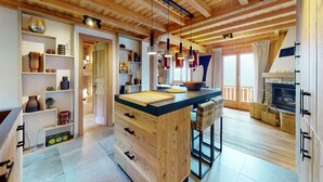 A spacious kitchen with wooden beams, a central island, and a fireplace. - Beautiful chalet in Le Bouveret with garden (Les Masses)