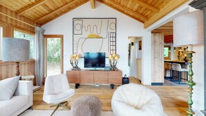 A spacious living area with a wooden ceiling, a large abstract painting, a flat-screen TV, and a cozy seating arrangement. - Beautiful chalet in Le Bouveret with garden (Les Masses)
