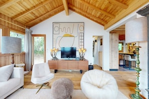Un vaste espace de vie agrémenté d’un plafond en bois, d’un grand tableau abstrait, d’un téléviseur à écran plat et d’un coin salon confortable.