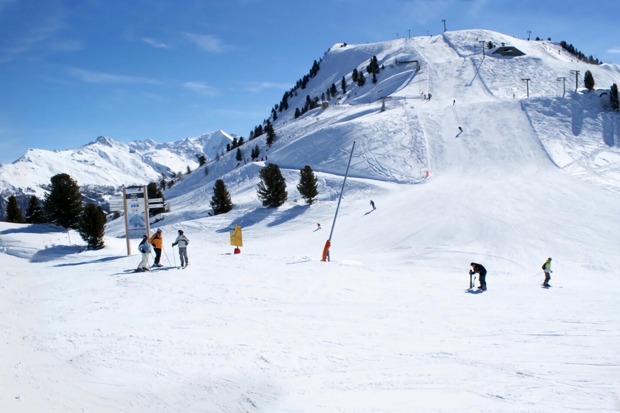 A snowy ski slope with skiers and a mountain backdrop.