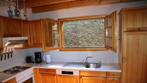 Een keuken met houten kastjes, een fornuis, een spoelbak en een raam met uitzicht op groen.
