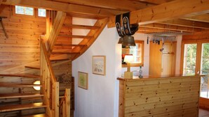 Een houten interieur met een trap, een keukenhoek met houten keukenkastjes en een hangklok in de keuken.