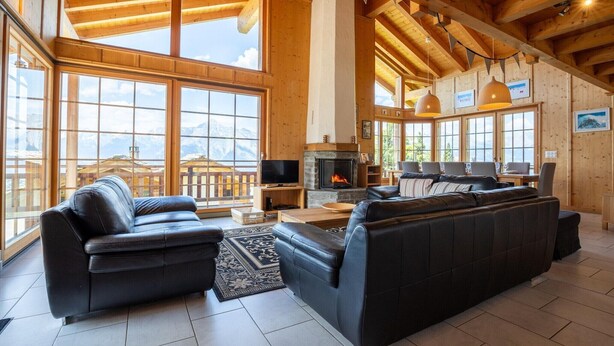 Ein geräumiges Wohnzimmer mit Kamin, Ledersofas und großen Fenstern mit Blick auf die Berge.