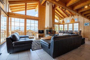 Un salon spacieux doté d’une cheminée, de canapés en cuir et de grandes fenêtres offrant une vue sur les montagnes.