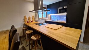 A modern kitchen with a wooden island, black cabinets, stainless steel appliances, and a window. - Family apartment with terrace (Veysonnaz)