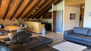 A modern living room with a wooden ceiling, a sofa, a coffee table, and a kitchen area in the background. - Family apartment with terrace (Veysonnaz)