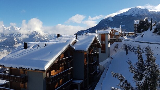 A snow-covered mountain village with wooden buildings and a clear view of snow-capped peaks in the background. - Family apartment with terrace (Veysonnaz)