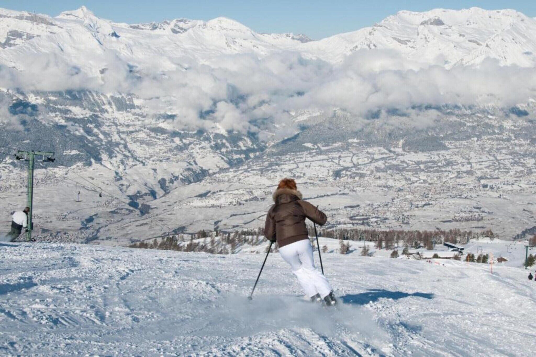 A person skiing down a snowy slope with a mountain range in the background.
