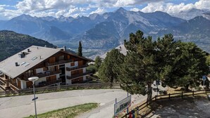 A mountain lodge with a wooden facade, a balcony, and a view of snow-capped mountains. - Cosy apartment in a central location (Veysonnaz)