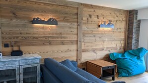 A cozy room with a wooden wall, a blue sofa, a small wooden table, and a teal bean bag. - Cosy apartment in a central location (Veysonnaz)