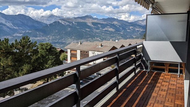 A balcony with a view of mountains, a wooden floor, and a metal railing. - Cosy apartment in a central location (Veysonnaz)