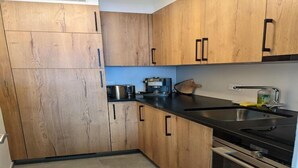 A modern kitchen with wooden cabinets, a black countertop, and stainless steel appliances. - Cosy apartment in a central location (Veysonnaz)