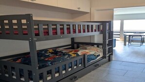 A bunk bed with a lower bunk and a pull-out desk, white cabinets above, and a view of a balcony with a chair. - Cosy apartment in a central location (Veysonnaz)