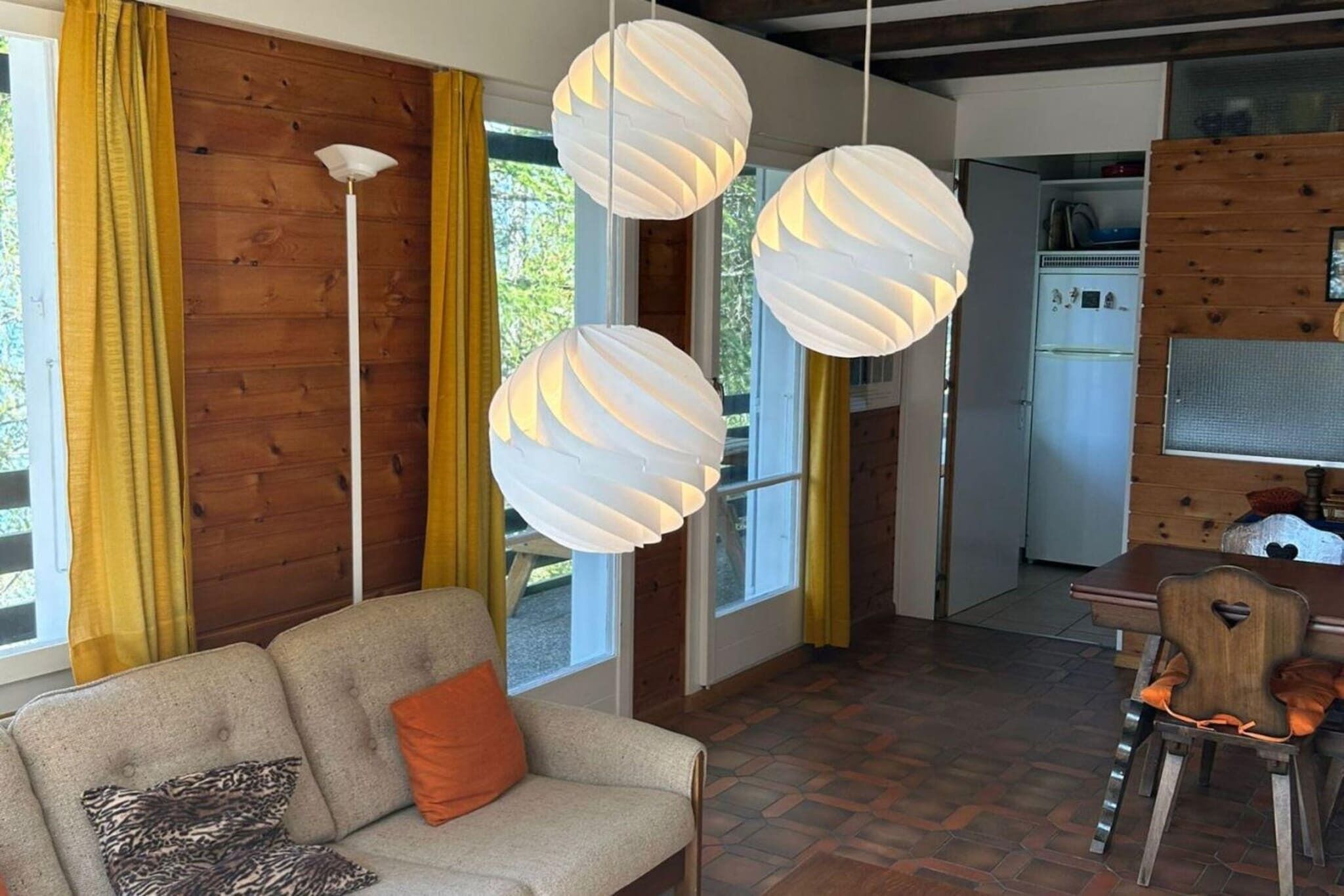 Una sala de estar con un sofá, una mesa de comedor con sillas, y una cocina al fondo.