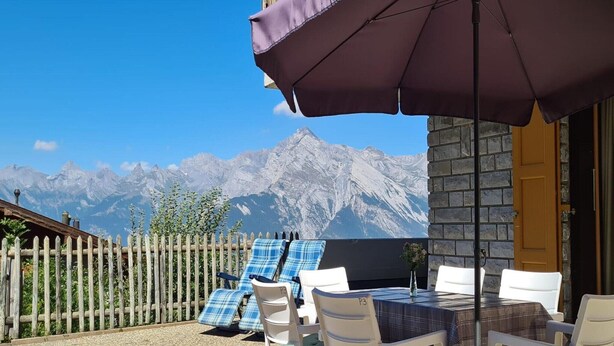 Une terrasse avec une table et des chaises, une clôture en bois et une vue sur la montagne.