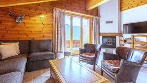 Un salon chaleureux avec un plafond en bois, une cheminée, un téléviseur et un canapé.