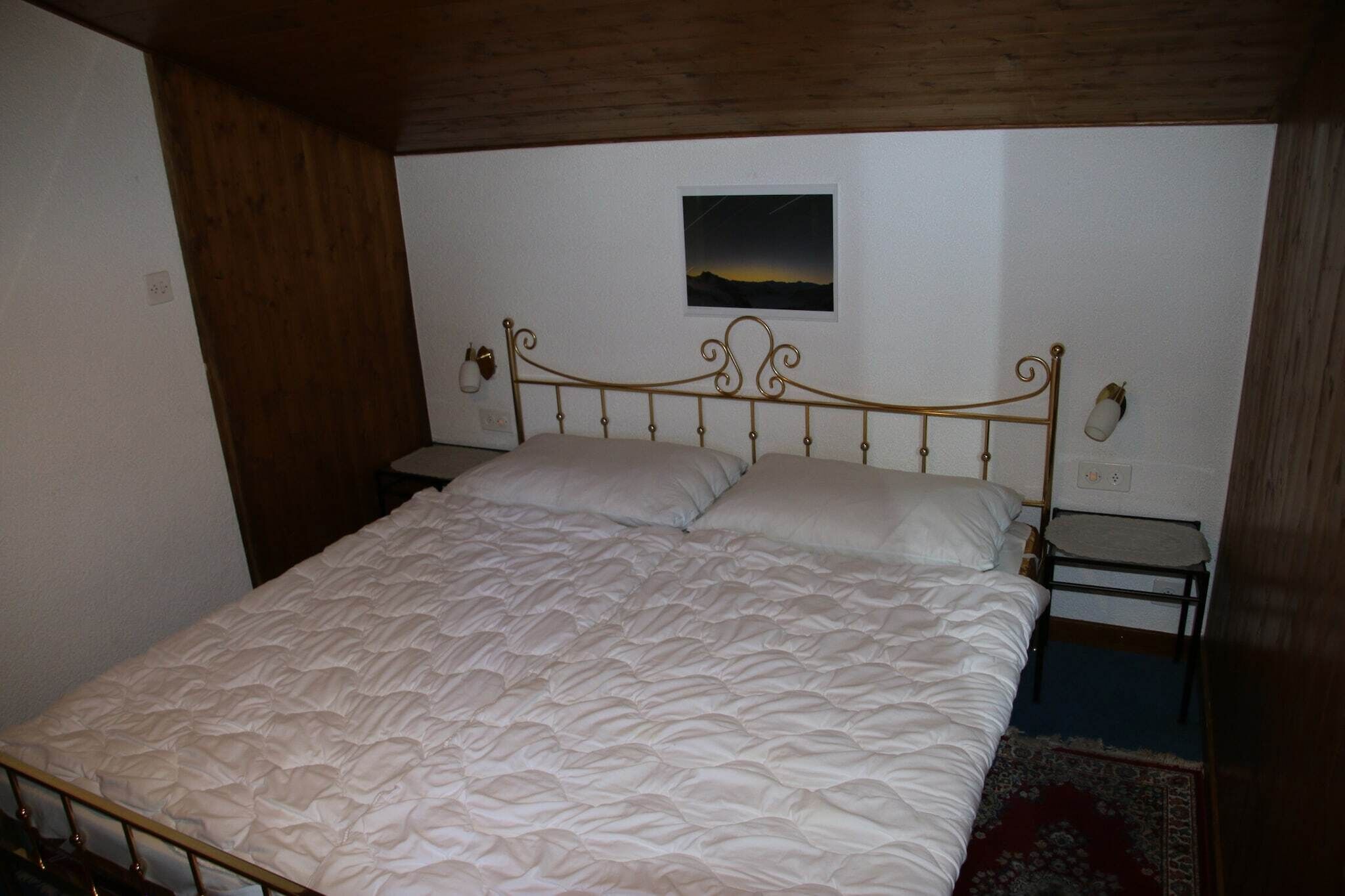 Una cama individual con estructura metálica y colcha blanca acolchada.