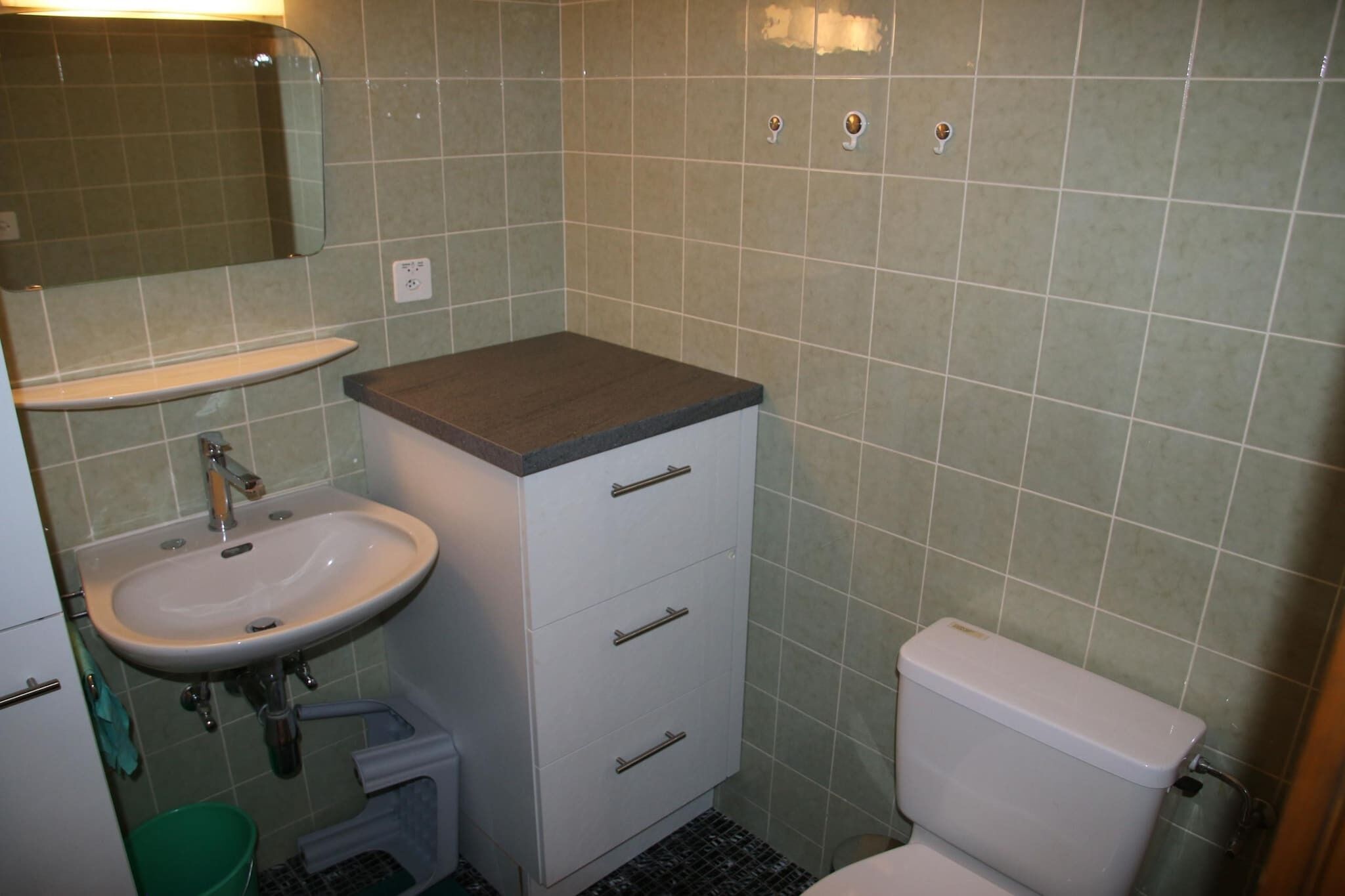 Un baño pequeño con lavamanos, espejo, mueble y retrete.