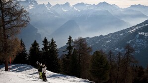 A snowy mountain landscape with skiers and a forested area.