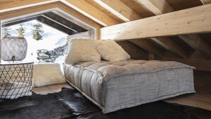 A cozy attic bedroom with a bed, a window with a view of snow-covered trees, and a small window seat with a basket. - Chalet in Les Masses with garden (Les Masses)