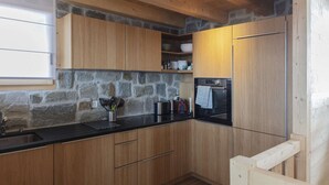 A kitchen with wooden cabinets, a stone wall, a black countertop, and a built-in oven. - Chalet in Les Masses with garden (Les Masses)