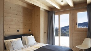 A wooden room with a bed, a chair, and a view of a mountainous landscape through a large window. - Chalet in Les Masses with garden (Les Masses)