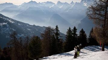 A snowy mountain landscape with skiers and a clear view of distant peaks.