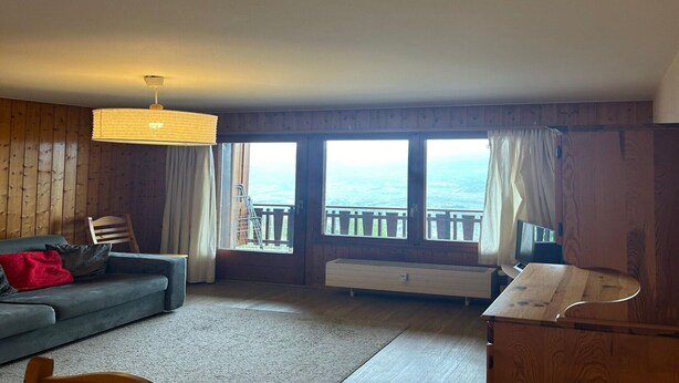A cozy living room with a sofa, a wooden cabinet, and a large window offering a view of the sea.