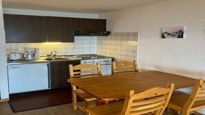 A compact kitchen with a dining area, including a refrigerator, stove, and wooden chairs.
