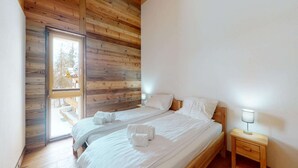 Un dormitorio con dos camas, paredes de madera, una ventana y una mesita de noche con lámpara.