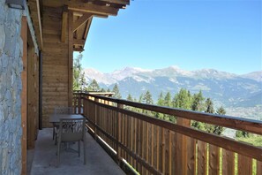 Enjoy breathtaking views of snow-capped mountains from this balcony with a table and two chairs.