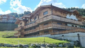 Una cabaña de madera de varios pisos con balcones, ubicada frente a montañas.