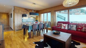 A spacious living area with a red sofa, a dining table, and a kitchen in the background. - Luxurious apartment in Veysonnaz (Veysonnaz)