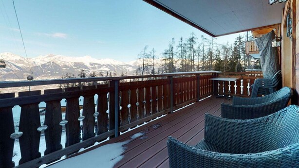 A wooden deck with wicker furniture and a view of snow-capped mountains. - Luxurious apartment in Veysonnaz (Veysonnaz)