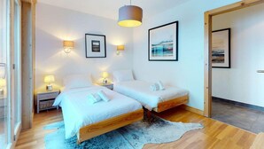 A modern bedroom with two single beds, bedside lamps, framed artwork on the walls, and a wooden floor. - Luxurious apartment in Veysonnaz (Veysonnaz)