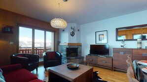 A cozy living room with a fireplace, a television, and a dining area with a wooden table and chairs. - Luxurious apartment in Veysonnaz (Veysonnaz)
