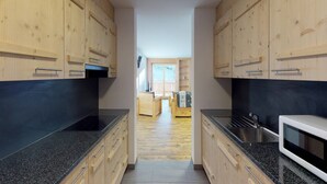 Une cuisine étroite, dotée de meubles en bois et de plans de travail noirs, qui donne sur un balcon offrant une vue agréable.