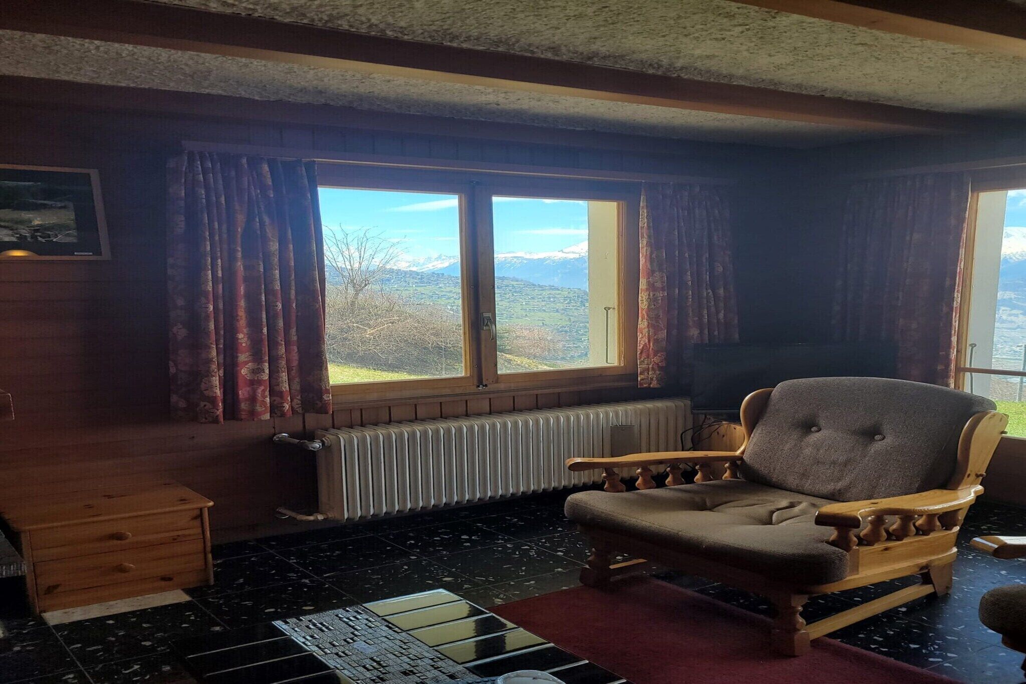 Una habitación acogedora con una silla de madera, un radiador y una ventana con cortinas.