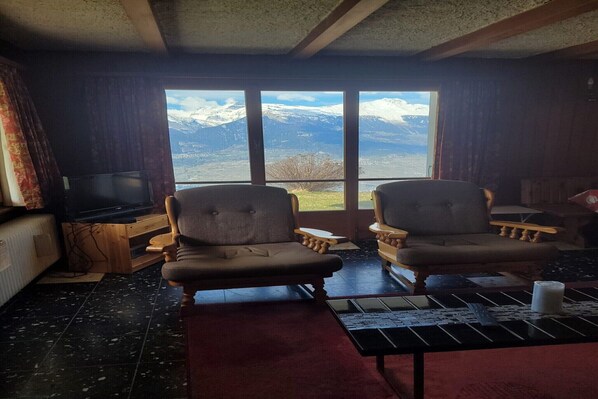 Une pièce avec deux fauteuils placés face à une grande fenêtre donnant sur un paysage de montagne.