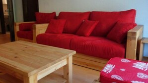 A red sofa with multiple cushions, a wooden coffee table, and a matching ottoman. - Modern apartment with sauna (Veysonnaz)