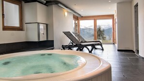 A spa area with a hot tub, lounge chairs, and a view of mountains through large windows. - Modern apartment with sauna (Veysonnaz)