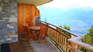 A wooden deck with a table and chairs, overlooking a mountainous landscape. - Modern apartment with sauna (Veysonnaz)