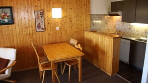 A compact kitchen with wooden walls, a dining table, chairs, a small island with a sink, and a dishwasher. - Apartment with Rhone valley view (Veysonnaz)