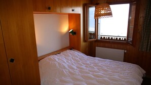 A wooden room with a bed, a window with a view, and a hanging light fixture. - Apartment with Rhone valley view (Veysonnaz)