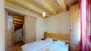 A wooden bedroom with two beds, a staircase, and a hanging light fixture.