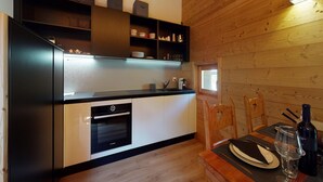 A modern kitchen with black and white cabinetry, a built-in oven, and a dining area with wooden chairs and a table set for two.