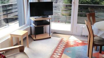 Una habitación con una televisión sobre un mueble bajo, una mesita, una silla y una alfombra colorida.