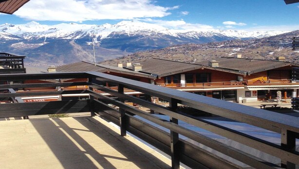 Un hotel con varias construcciones, un balcón de madera y una montaña nevada al fondo.