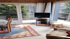 Una habitación acogedora con un televisor sobre un mueble bajo, una silla de madera, una mesita pequeña y una alfombra colorida.