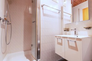 A modern bathroom with a glass shower enclosure, a white sink with a mirror above, and a wooden ceiling. - 3-bedroom apartment in Veysonnaz (Veysonnaz)